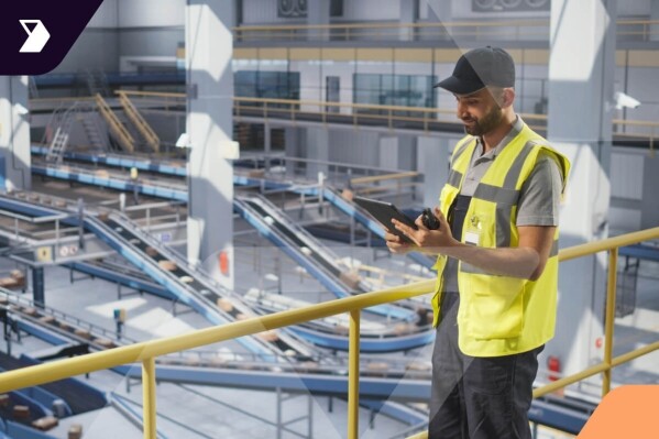 Warehouse supervisor on an elevated platform uses a tablet, overlooking an automated sorting and conveyor system