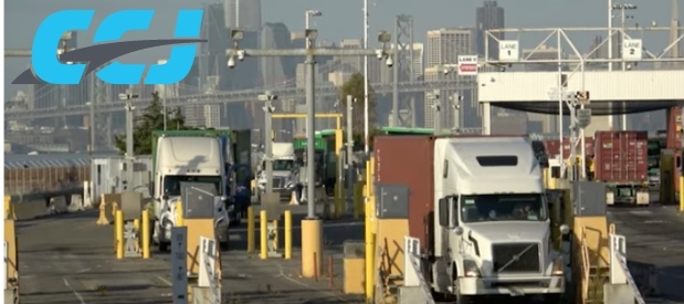 Semi-trucks with cargo containers drive through lanes at a port or shipping terminal, with a city skyline and bridge in the background. The blue CCJ logo appears in the upper left corner.